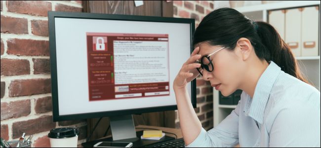 Woman who looks upset sitting next to a computer monitor with ransomware on it.