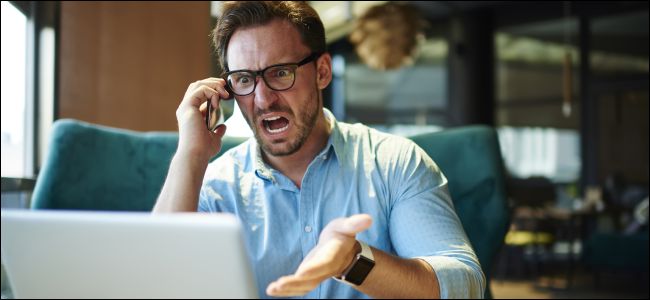 Upset man on cell phone gesturing at a laptop.