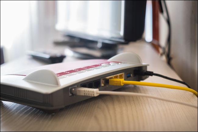 Cables plugged into the back of a modem that is sitting on a desk next to a computer.